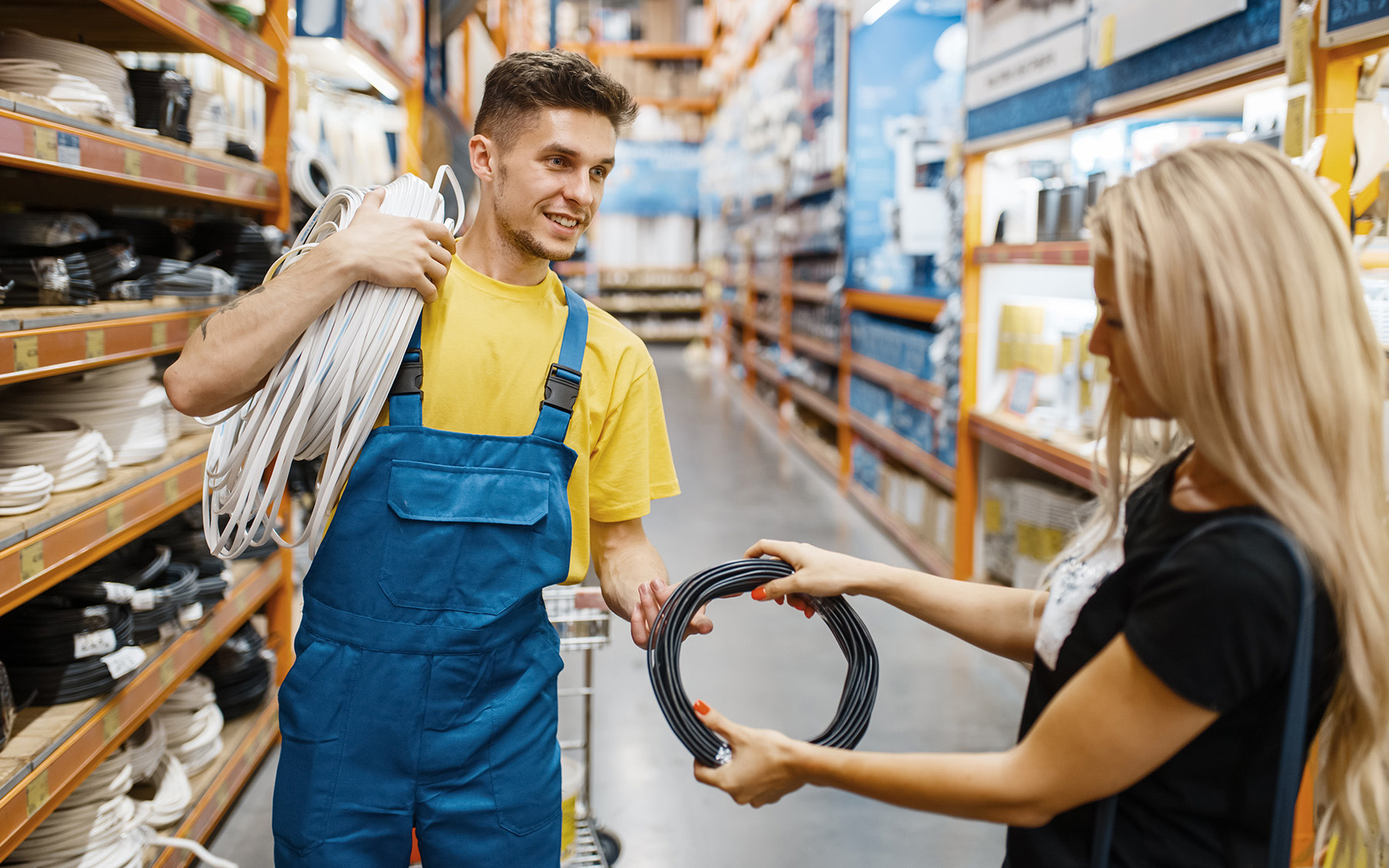 Assistant and female customer with wires in hardware store. Seller in uniform and woman in diy shop, shopping in building supermarket