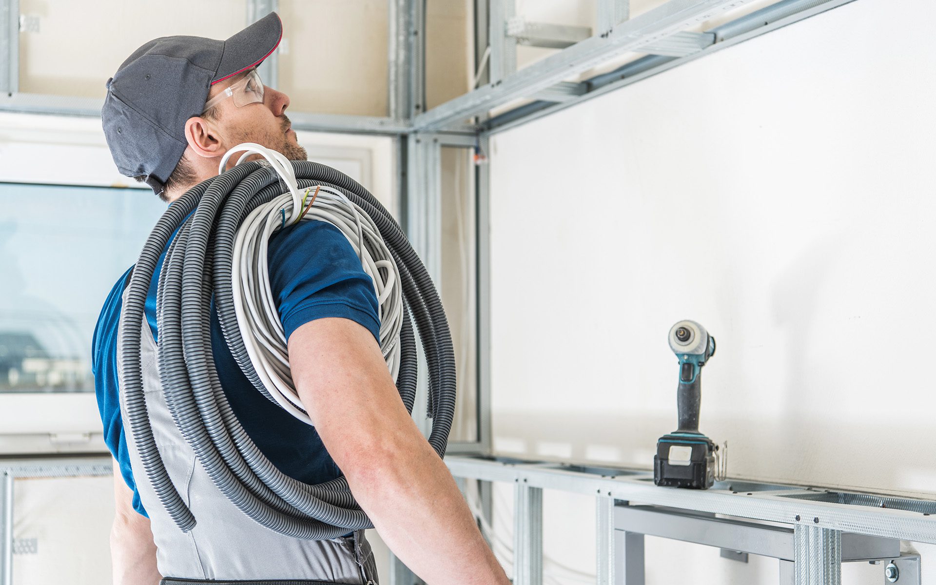 Electrician Ready For Work. Caucasian Electric Worker in His 30s with Pile of Cables on His Shoulder.
